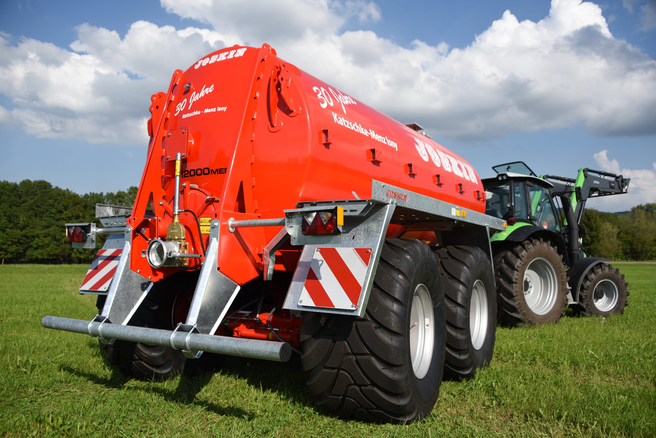 Rotes JOSKIN-Jubiläumsfass von schräg hinten mit Traktor unter weißen Wolken
