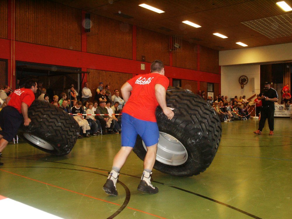 Athlet kippt einen großen Reifen mit Felge durch die Sporthalle