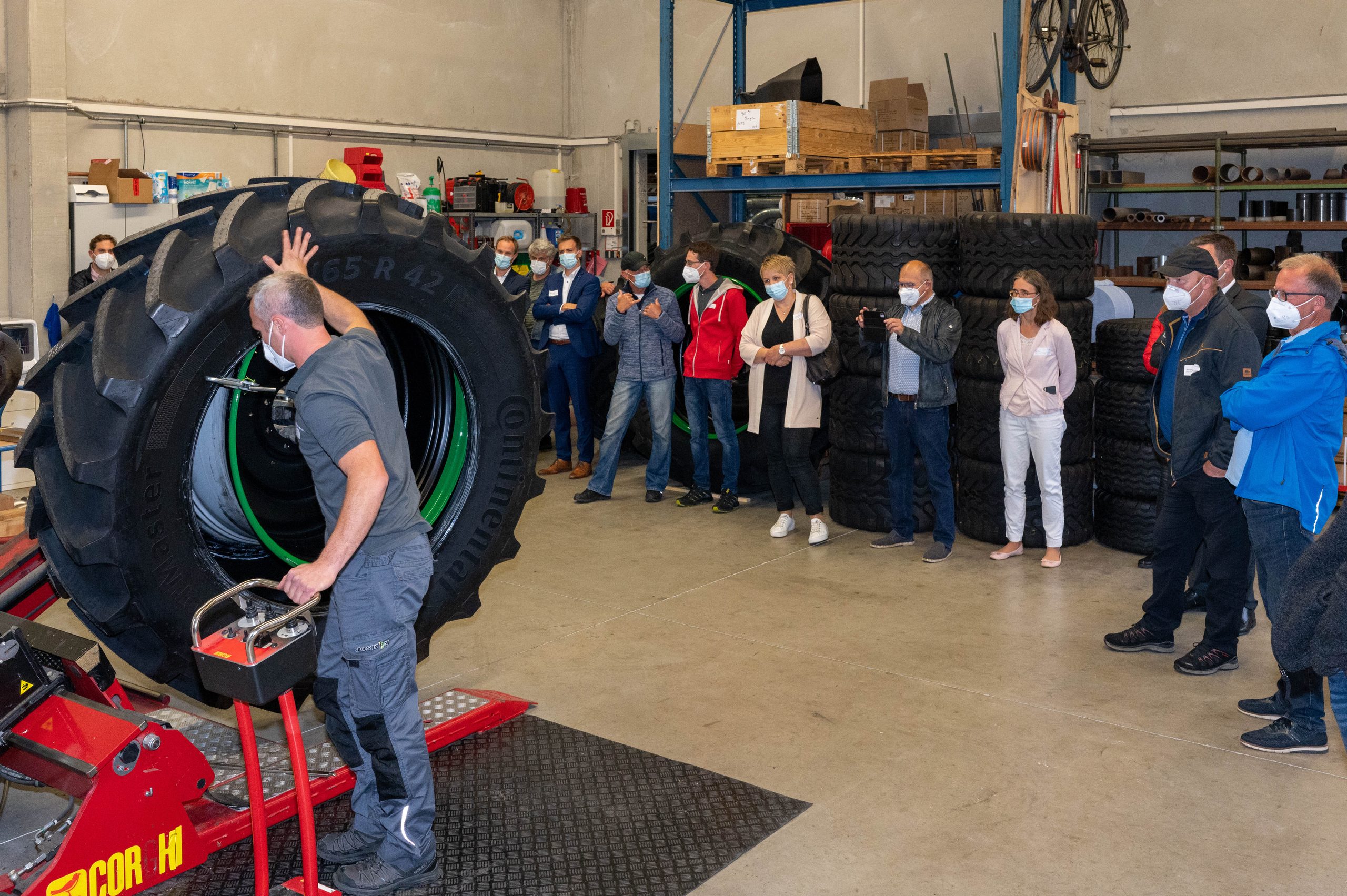 Mitarbeiter zeigt den Gästen in der Werkstatt die Montage eines großen Traktorreifens