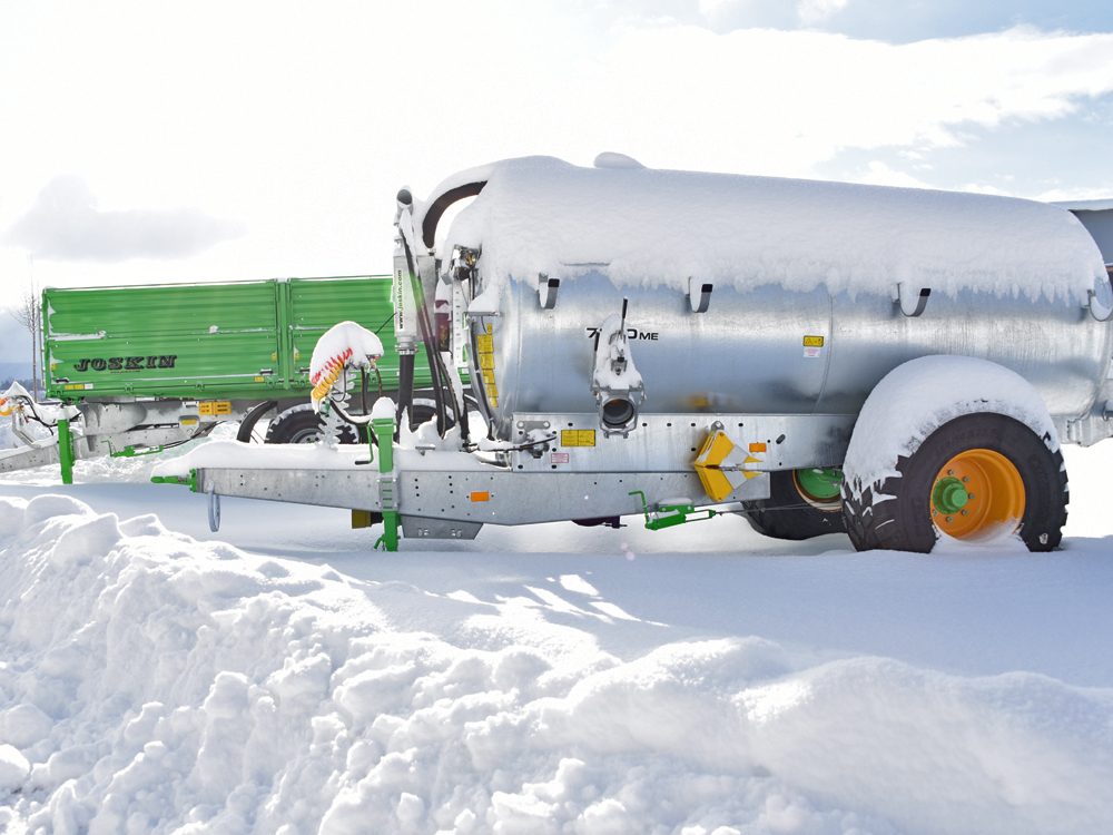 JOSKIN-Güllefass tief im Schnee vor einem grünen Kipper
